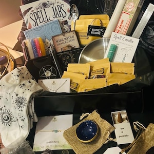 May include: A black box filled with various spiritual items. Includes a book titled "Spell Jars", oracle cards, candles, incense, a small bowl, and other mystical supplies. The box also contains a small sign that reads "Witches Welcome".