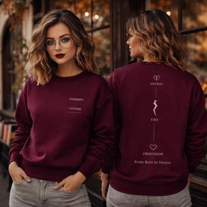 Può includere: Felpa bordeaux con le parole "ENEMIES LOVERS" stampate sul davanti. Il retro della felpa presenta le parole "HATRED FIRE OBSESSION From Ruin to Desire" con simboli grafici. La felpa è di colore pieno.