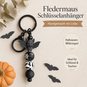 Könnte beinhalten: Ein schwarzer Schlüsselanhänger mit einem fledermausförmigen Anhänger und drei runden Perlen. Die Perlen umfassen eine Perle mit weißem Blumenmuster auf schwarzem Grund, eine mit weißem Fledermausmuster und eine einfarbig schwarze Perle.