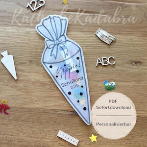 Puede incluir: Una bolsa de regalo transparente en forma de cono, atada con un lazo, llena de confeti y un lápiz. La bolsa tiene la inscripción "Gippie! Schulkind 2026". Recortes de madera de letras, números y formas rodean la bolsa.