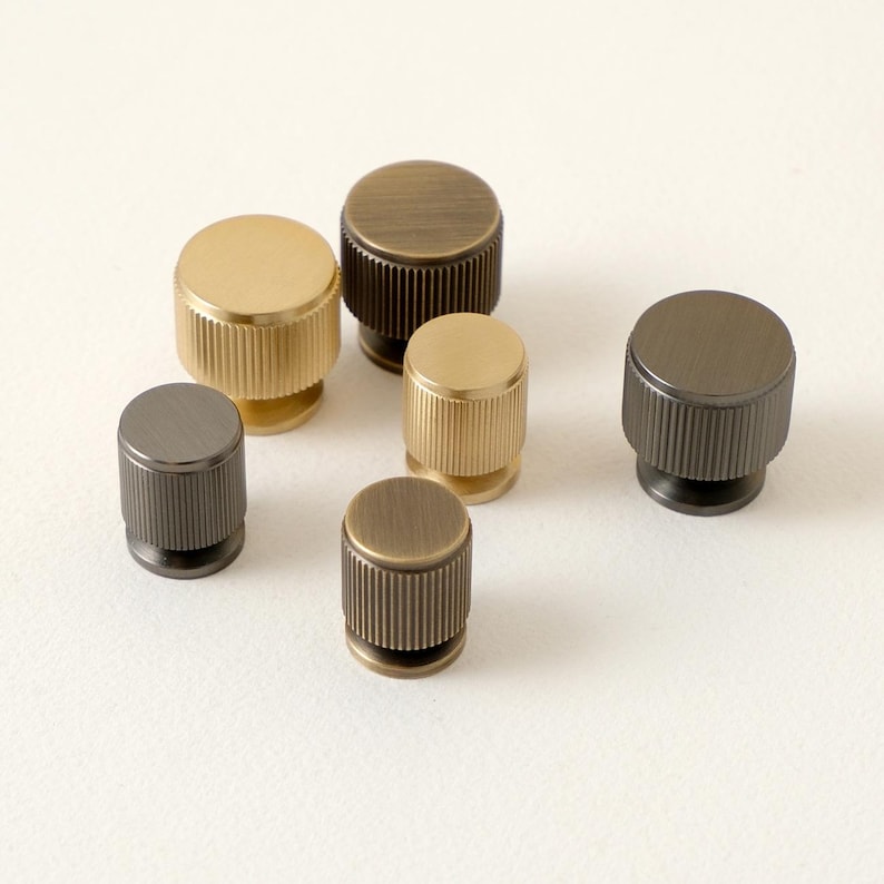 Peut inclure: Ensemble de six boutons de meubles m&eacute;talliques aux finitions vari&eacute;es, or, bronze et gris fonc&eacute;. Chaque bouton a une forme cylindrique avec une texture stri&eacute;e sur les c&ocirc;t&eacute;s et un dessus plat. Mesures en centim&egrave;tres.