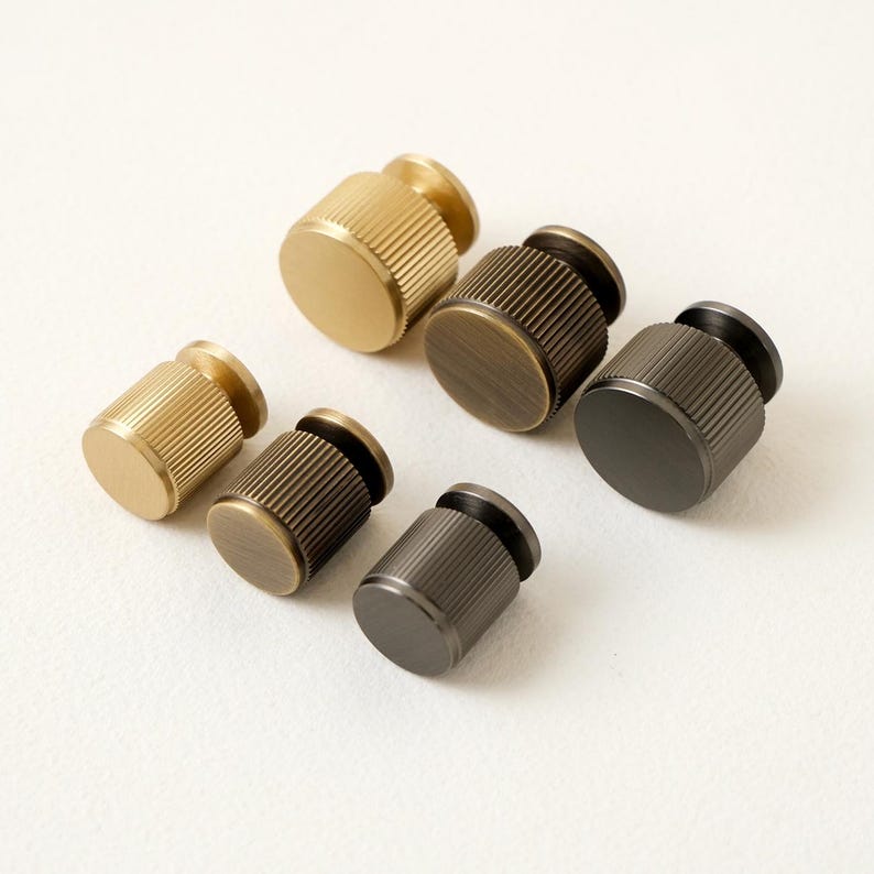 Peut inclure: Six boutons de meubles cylindriques en finitions m&eacute;talliques vari&eacute;es : or, bronze et gris fonc&eacute;. Chaque bouton pr&eacute;sente un corps cannel&eacute; et un dessus et une base plats, pour meubles ou d&eacute;coration.