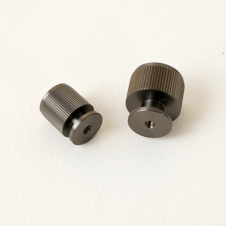 Peut inclure: Deux boutons en m&eacute;tal gris fonc&eacute;. Chaque bouton a un corps cylindrique avec une texture stri&eacute;e et une base circulaire. La base comporte un trou filet&eacute;. Ces boutons sont adapt&eacute;s aux meubles ou &agrave; la quincaillerie d'armoires.