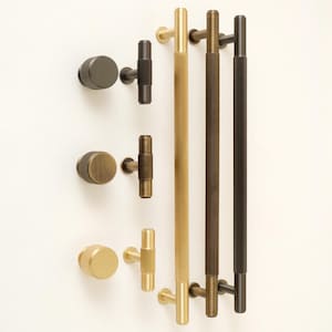 Peut inclure: Une collection de quincaillerie d'armoires, comprenant des boutons et des poignées, dans diverses finitions métalliques. Les boutons sont ronds avec une texture striée, tandis que les poignées sont longues et cylindriques. Les finitions incluent le laiton, le bronze et le noir.