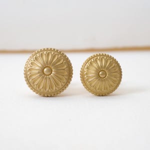 Puede incluir: Dos pomos de armario redondos de color dorado. Cada pomo presenta un diseño floral detallado con un botón central y un borde con cuentas. Los pomos son de metal, probablemente para muebles.
