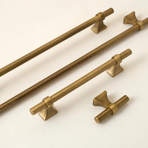 Peut inclure: Ensemble de quincaillerie de meubles en laiton antique, comprenant plusieurs barres de tirage et un bouton. Les barres ont un design cylindrique avec des supports carrés. L'ensemble est sur fond blanc.