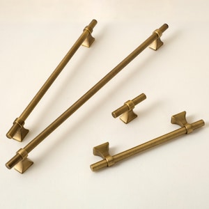 Op de afbeelding: Een verzameling antieke messing kastbeslagen, waaronder lange stangtrekkers en kleinere knoppen. De hardware heeft een warme, verouderde afwerking en een klassiek ontwerp, geschikt voor keuken- of badkamerkasten. De trekstangen zijn ongeveer 30 cm lang.