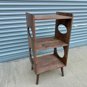 Op de afbeelding: Een houten kattenplank met drie niveaus en ronde uitsparingen. De plank is gemaakt van donkerbruin hout en heeft een modern design uit het midden van de eeuw. Ontworpen als kattenboom.