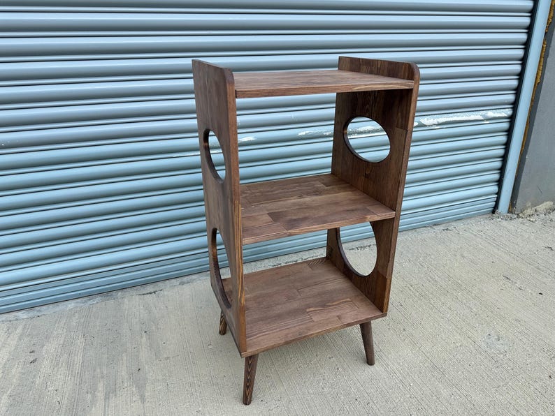 Op de afbeelding: Een houten kattenplank met drie niveaus en ronde uitsparingen. De plank is gemaakt van donkerbruin hout en heeft een modern design uit het midden van de eeuw. Ontworpen als kattenboom.