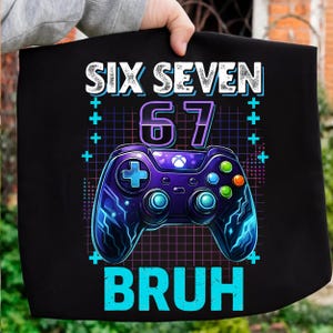 May include: Black graphic tee with the text "SIX SEVEN 67 BRUH" in white and teal. The design includes a purple video game controller with blue and orange buttons, set against a grid background.