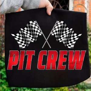 Może przedstawiać: Czarna torba z dwoma skrzyżowanymi szachownicami wyścigowymi. Słowa "PIT CREW" są wydrukowane na czerwono, ze śladami opon. Torba jest trzymana przez osobę.