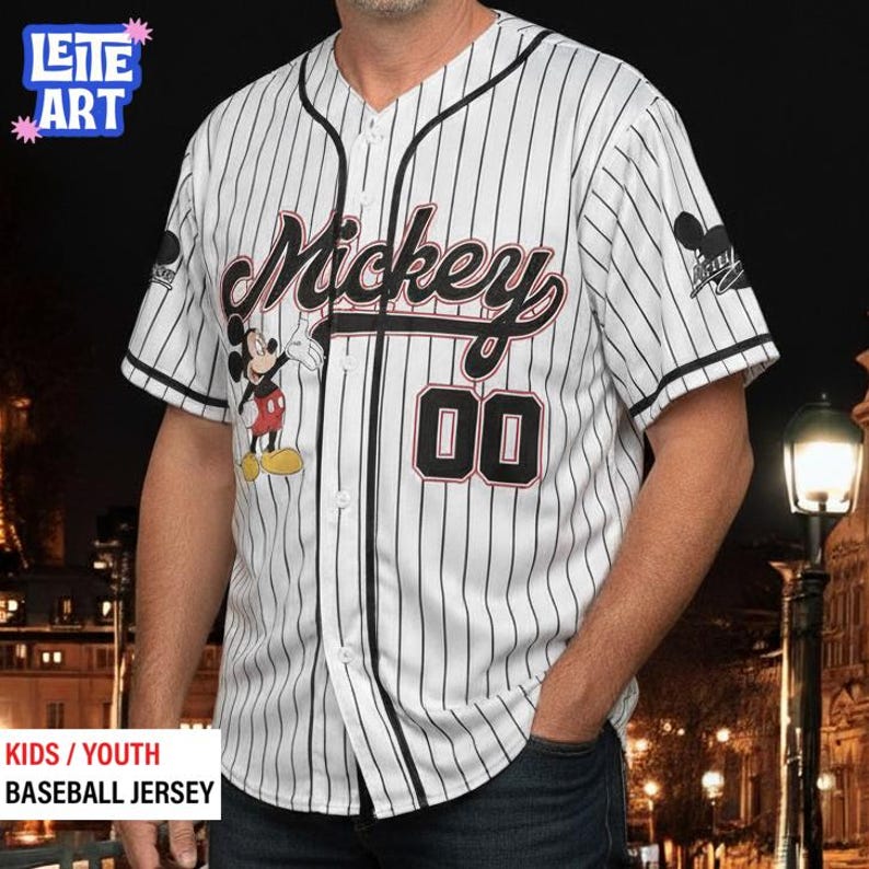 A man wearing a Mickey Mouse baseball jersey with the number 00, standing in front of a nighttime cityscape.
