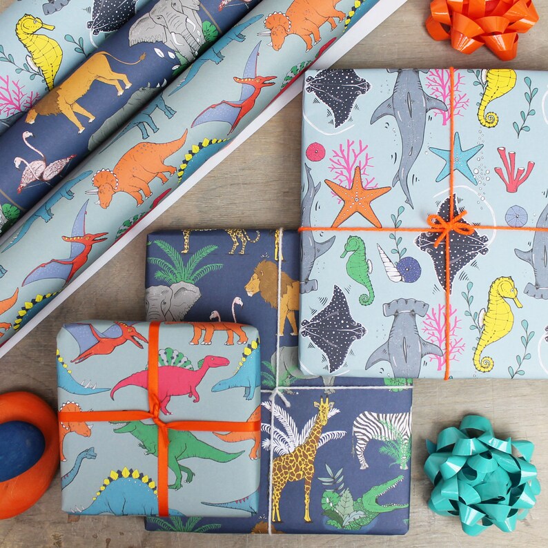 May include: An assortment of wrapped gifts and rolls of wrapping paper with colorful illustrations of dinosaurs, sea creatures, and jungle animals. The gifts are tied with orange ribbons and bows, and the paper has a light blue and navy background.