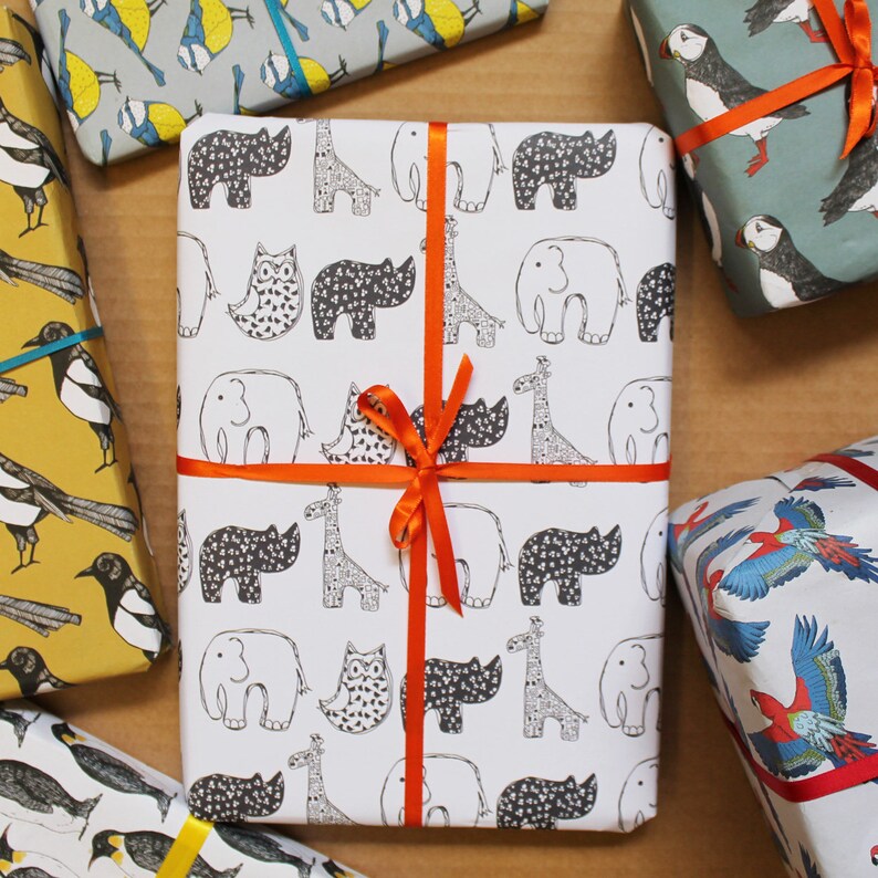 Op de afbeelding: Wit inpakpapier met een herhalend zwart-wit patroon van neushoorns, uilen, giraffen en olifanten. Het papier is vastgebonden met een fel oranje lint.