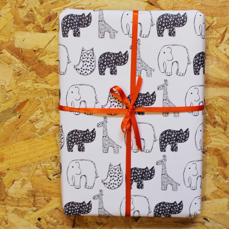 Op de afbeelding: Wit inpakpapier met een herhalend patroon van zwart-witte neushoorns, giraffen, olifanten en uilen. Het papier is vastgebonden met een feloranje lint.