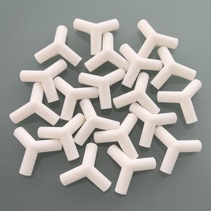 May include: A collection of white, Y-shaped plastic connectors. Each piece has three cylindrical arms extending from a central point. The connectors are arranged on a gray surface, creating a visually interesting pattern.