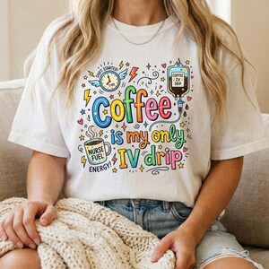 May include: White t-shirt with a colorful graphic that reads "Coffee is my only IV drip." The design includes a coffee cup, IV bag, and a clock. The shirt is a casual, comfortable style.