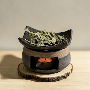 Puede incluir: Una taza de cerámica blanca con asa negra y el texto "But First, Coffee" en negrita negra. La taza está sobre un fondo borroso. La taza mide aproximadamente 10 cm de altura.