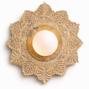 May include: Ornate, beige-colored wall sconce with a central, frosted glass globe. The sconce features a detailed, floral-inspired design around a gold-colored circular base. The light fixture is designed to be mounted on a wall.