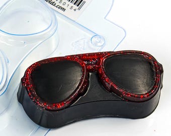 Könnte beinhalten: Eine schwarze Sonnenbrillenform mit roten Glitzerakzenten. Die Sonnenbrille hat eine klassische Aviator-Form und ist auf einer transparenten Kunststoffform platziert. Das Bild ist gut beleuchtet.