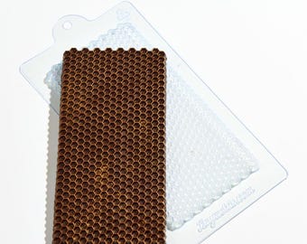 May include: A brown honeycomb-patterned chocolate bar next to a clear plastic mold. The mold has a honeycomb pattern on one side and a smooth surface on the other. The chocolate bar is rectangular and has a detailed honeycomb design.