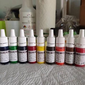 May include: A row of small, colorful pigment bottles for soap making. The bottles are white with white caps and contain various colors, including blue, green, red, and yellow. The labels read "PIGMENT FOR SOAP".