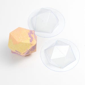 Może przedstawiać: Geometryczna kula do kąpieli w odcieniach żółtego, pomarańczowego i fioletowego, obok dwóch przezroczystych plastikowych foremek. Kula do kąpieli ma fasetowany kształt. Formy są okrągłe z geometrycznym kształtem w środku.