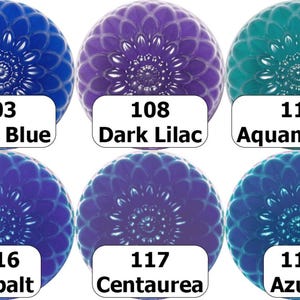 May include: Six decorative glass cabochons in shades of blue, purple, and teal. Each cabochon has a floral design and a white label with a color name and number. Colors include Dark Blue, Dark Lilac, Aquamarine, Cobalt, Centaurea, and Azure.