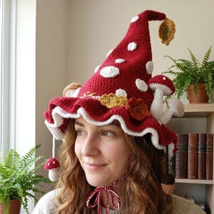 Puede incluir: Un sombrero de ganchillo hecho a mano con diseño de seta. El sombrero es principalmente rojo con lunares blancos y un borde con volantes. Cuenta con setas, hojas y un lazo de ganchillo decorativos. Un accesorio único.