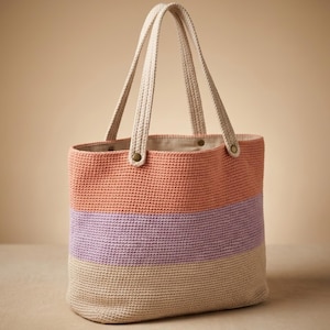 May include: A tote bag featuring a horizontal color-blocked design with sections of coral, lavender, and beige. The bag is constructed from a textured, woven material and includes two matching beige handles attached with small, circular brass-toned rivets.