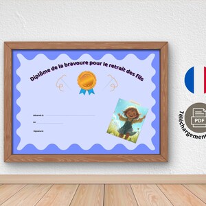 May include: A framed certificate with the text "Diplôme de la bravoure pour le retrait des fils" in blue, featuring a gold medal and a small illustration of a child. The frame is brown, and the background is a white wall.