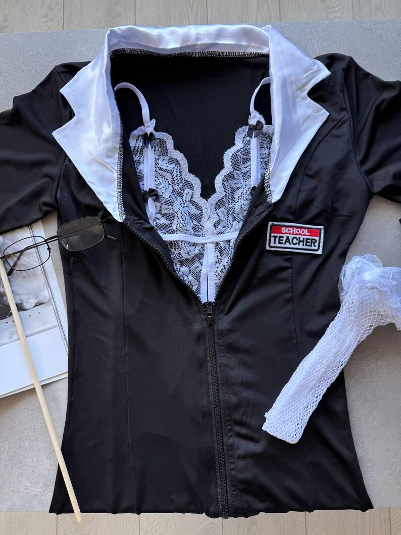 May include: Black lingerie set with a white lace bodice and a black jacket with white lapels. The jacket has a zipper closure and a "SCHOOL TEACHER" patch. Includes a pair of glasses and a white fishnet sleeve.