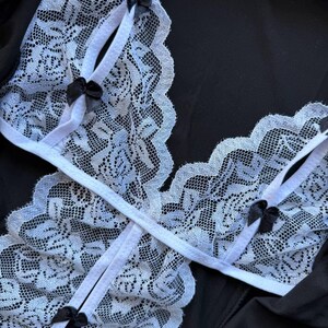May include: A black lingerie set featuring a white lace design with delicate black bows. The lace trim is scalloped, and the straps are white. The set is made of a soft, possibly silky material.