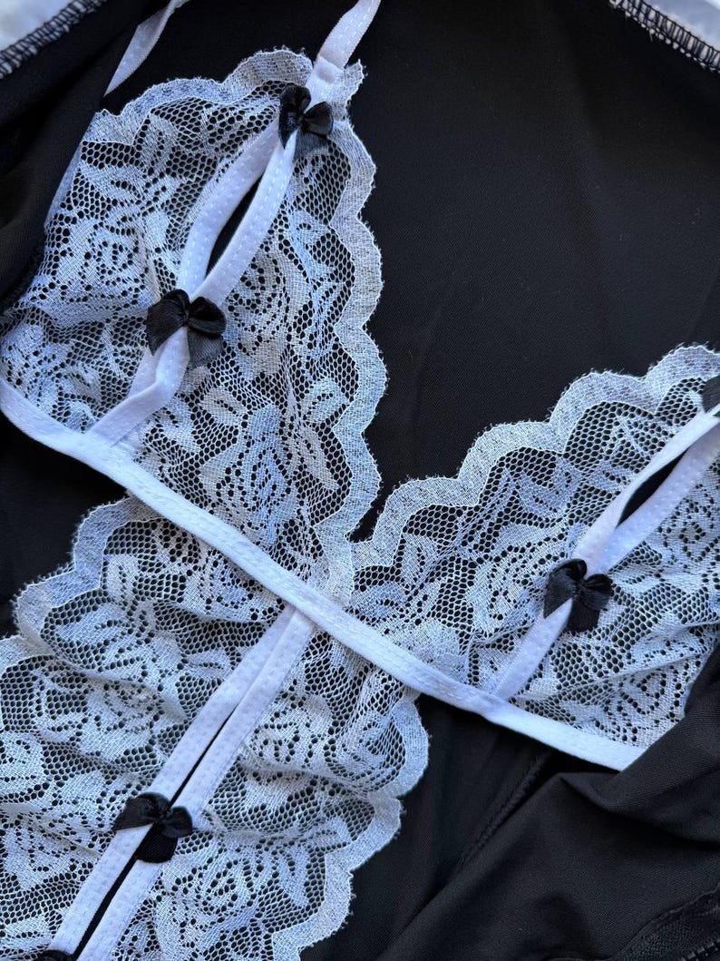 May include: A black lingerie set featuring a white lace design with delicate black bows. The lace trim is scalloped, and the straps are white. The set is made of a soft, possibly silky material.