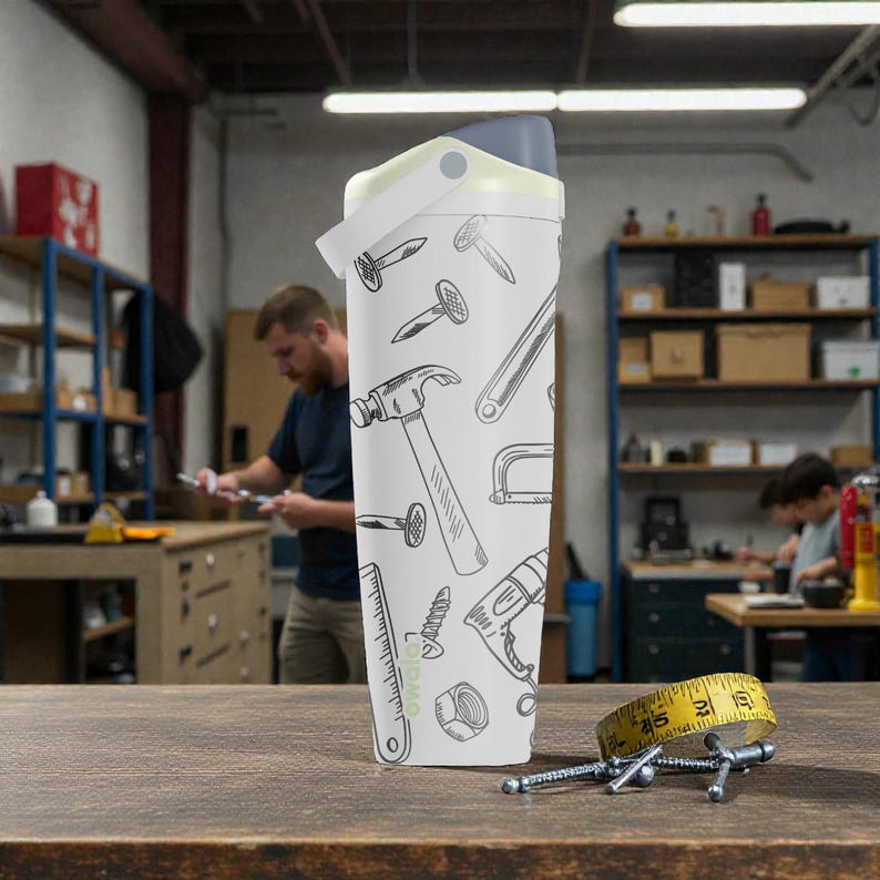 May include: A white water bottle with a gray lid and handle, decorated with black line drawings of tools. A yellow measuring tape and several screws are on the wooden surface in front of the bottle.