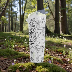Pu&ograve; includere: Borraccia bianca con un design floreale e colibr&igrave;. La borraccia ha un manico e un coperchio bianchi con la parte superiore grigia. Il design include illustrazioni in bianco e nero di fiori, colibr&igrave; e farfalle.