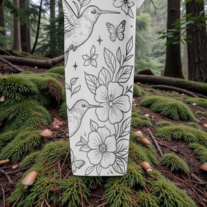 Pu&ograve; includere: Un bicchiere bianco con un design floreale in bianco e nero con colibr&igrave;, fiori e farfalle. Il bicchiere &egrave; ambientato su uno sfondo di foresta con muschio e funghi.