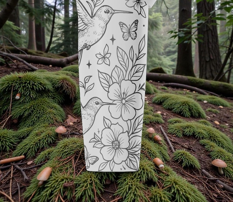 Pu&ograve; includere: Un bicchiere bianco con un design floreale in bianco e nero con colibr&igrave;, fiori e farfalle. Il bicchiere &egrave; ambientato su uno sfondo di foresta con muschio e funghi.
