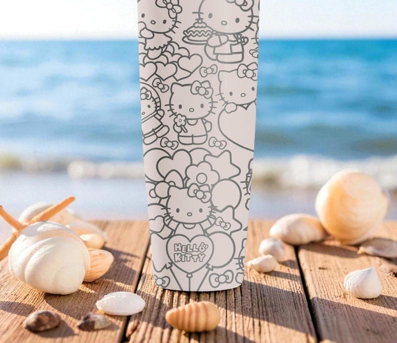 May include: A white tumbler featuring a black and white Hello Kitty design. The tumbler is covered in illustrations of Hello Kitty with hearts and bows. The tumbler is on a wooden surface with seashells and the ocean in the background.