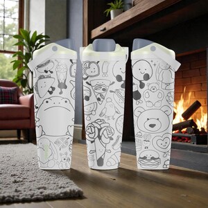 May include: Three white water bottles with gray lids and handles. Each bottle is covered in black and white cartoon illustrations of food and animals. The bottles are set against a blurred background of a fireplace and living room.