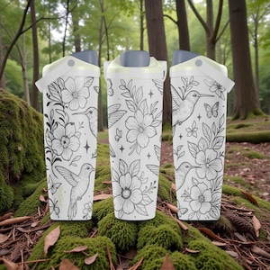 Pu&ograve; includere: Tre tazze da viaggio bianche con un design floreale e colibr&igrave;. Le tazze hanno un coperchio e un manico grigi. Il design presenta illustrazioni in bianco e nero di fiori, colibr&igrave;, farfalle e stelle. Le tazze sono ambientate su uno sfondo naturale della foresta.