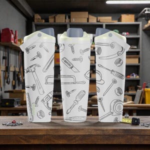 May include: Three white insulated tumblers with gray lids and a flip-top closure. Each tumbler is decorated with a repeating pattern of hand-drawn tools, including hammers, saws, and screwdrivers. The tumblers are displayed on a wooden surface.