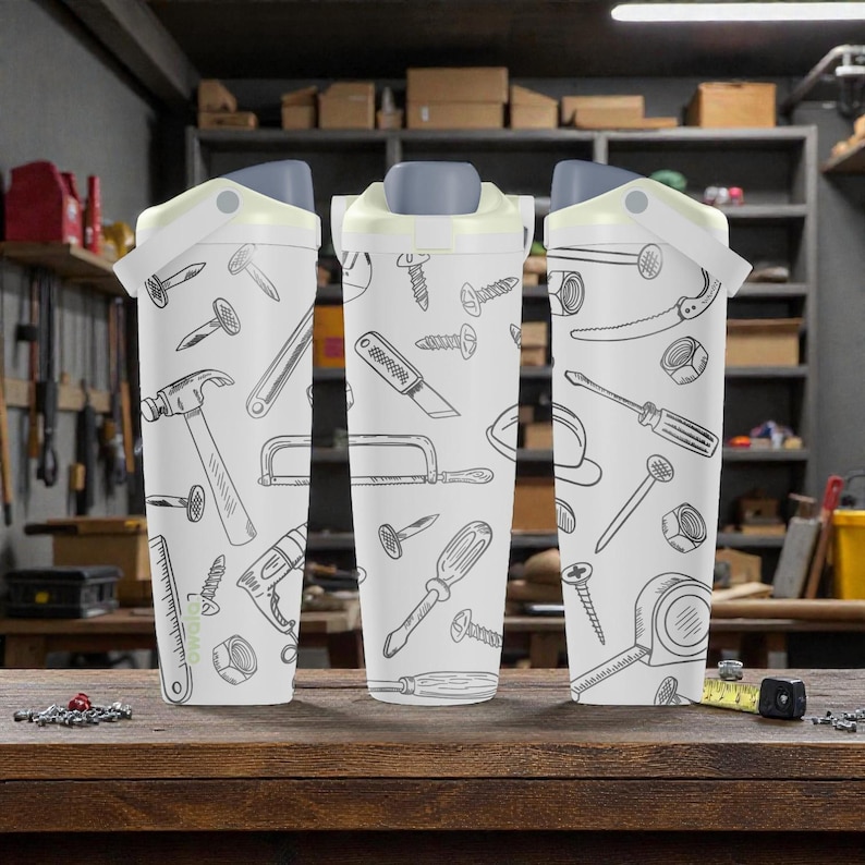 May include: Three white insulated tumblers with gray lids and a flip-top closure. Each tumbler is decorated with a repeating pattern of hand-drawn tools, including hammers, saws, and screwdrivers. The tumblers are displayed on a wooden surface.