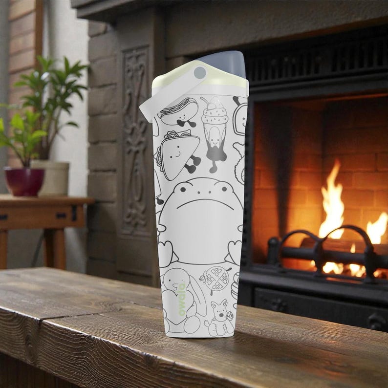 May include: White water bottle with a black and white cartoon design featuring a frog, hot dog, taco, and other food items. The bottle has a gray lid and a white handle. The bottle is sitting on a wooden surface.