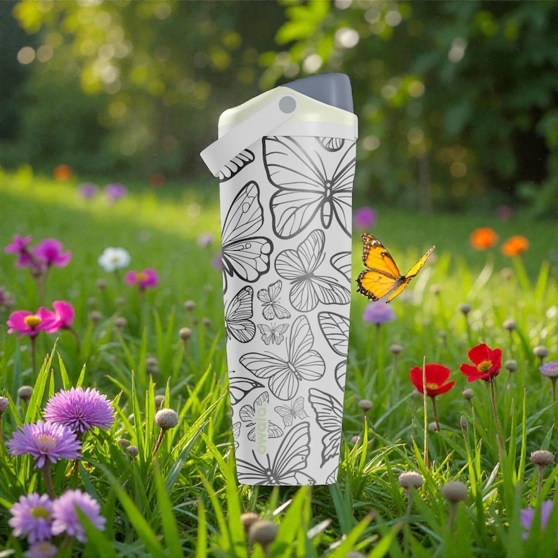 May include: A white water bottle with a gray lid and a butterfly pattern. The bottle is cylindrical and features a repeating design of black and white butterflies. The background is a field of green grass and colorful flowers.
