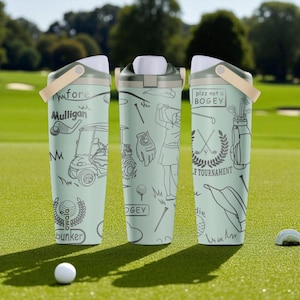 Puede incluir: Tres botellas de agua aisladas de color verde claro con ilustraciones y texto con temática de golf. Cada botella tiene una tapa blanca, un asa beige y dibujos lineales negros de equipos de golf y frases como "Mulligan" y "plzz not a BOGEY". Una pelota de golf descansa sobre el césped.