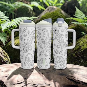 May include: Three white insulated tumblers with handles, featuring a black line art pattern of spotted lizards, leaves, flowers, and small hearts. Each tumbler has a light grey lid with a push-button mechanism and a tapered cylindrical body.