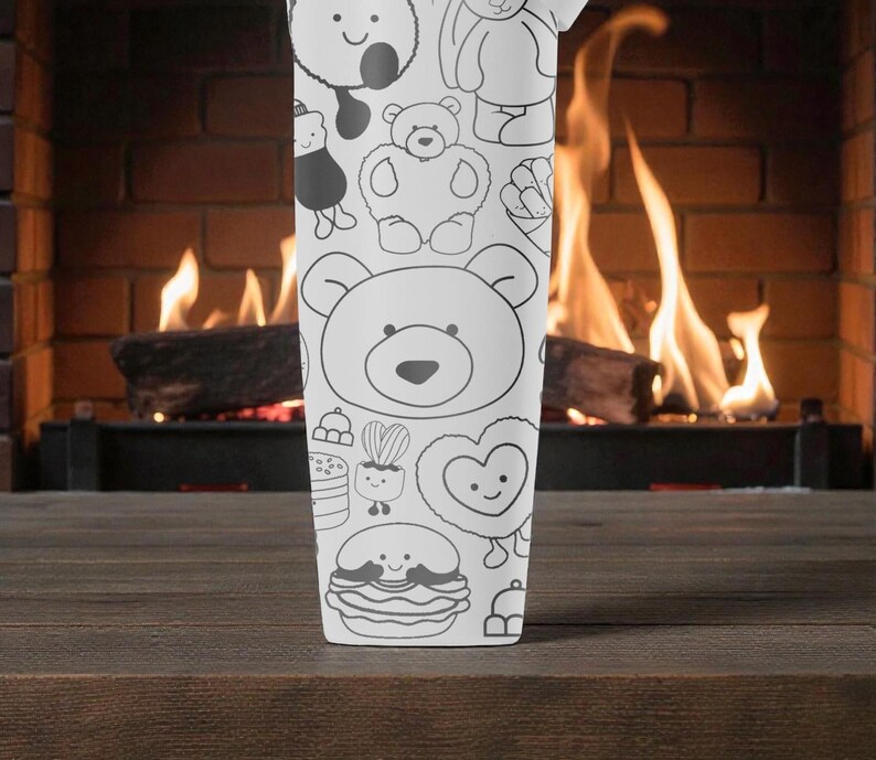 May include: A white tumbler featuring a repeating pattern of cartoon bears and other cute characters. The design is in black outline on a white background. The tumbler is set against a backdrop of a fireplace with a burning fire.