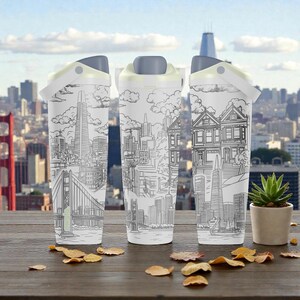 Puede incluir: Tres tazas de viaje blancas con un diseño de paisaje urbano de San Francisco en blanco y negro. Cada taza tiene una tapa gris y un asa de color amarillo claro. El fondo presenta el Golden Gate Bridge y un paisaje urbano.