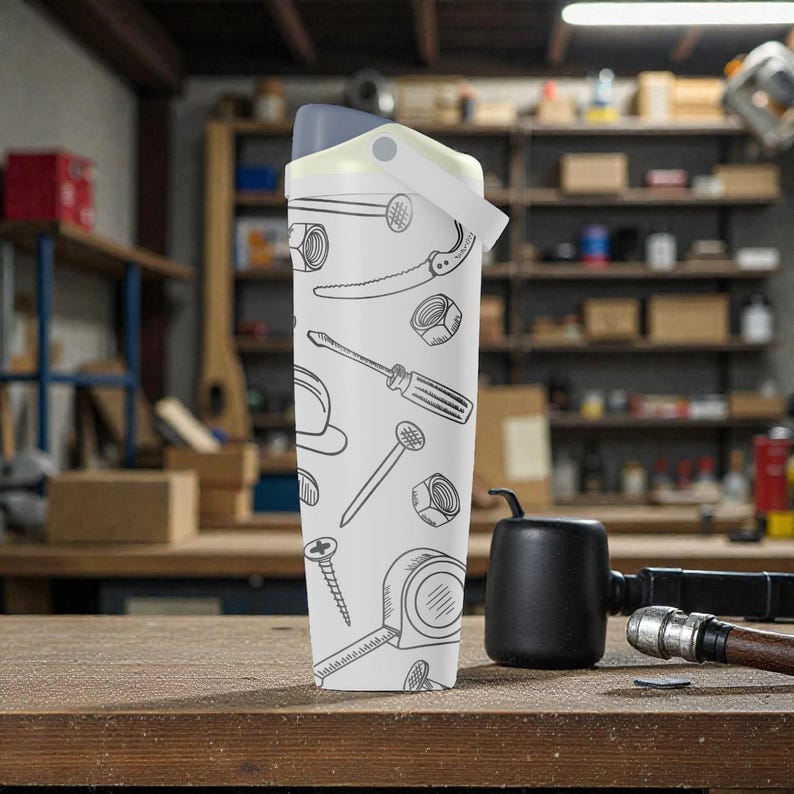 May include: A white water bottle with a gray lid and handle, decorated with black line drawings of tools like a saw, screwdriver, and tape measure. The bottle is standing on a wooden surface.